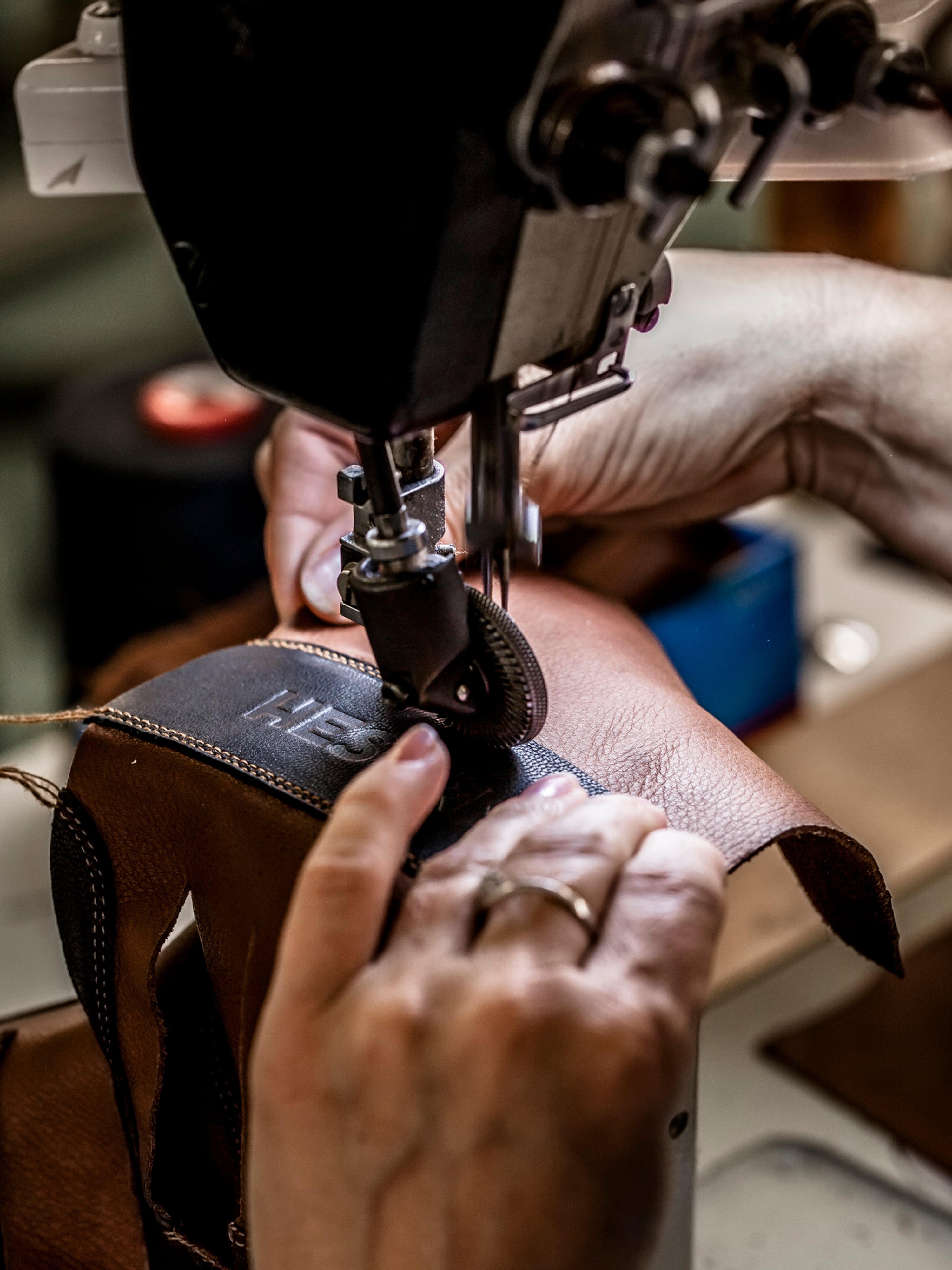 Close-up: hands stitching the Hestra logo onto a glove cuff on an industrial sewing machine